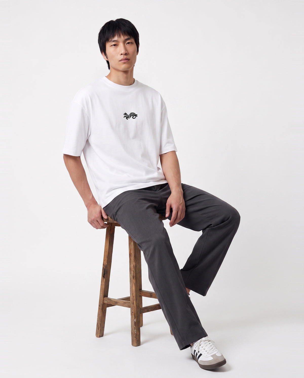 Model seated on a stool wearing the white Dear India oversized tee with the tiger logo