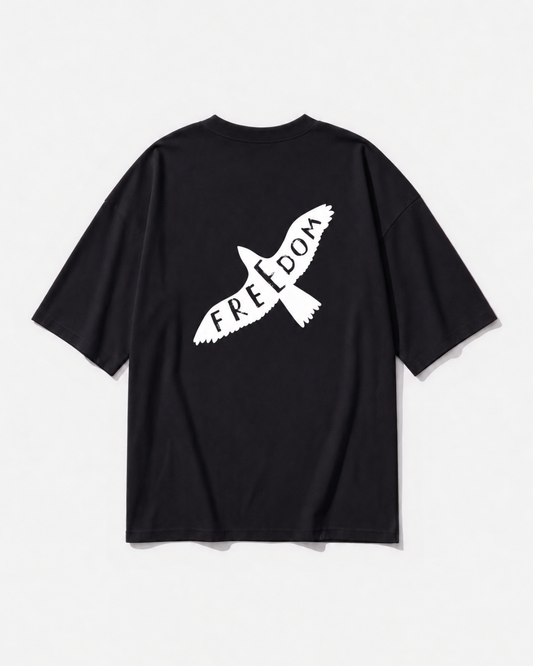 A bird in flight with FREEDOM lettered into its wings printed across the back of a black oversized t-shirt by Dear India