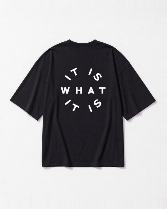 An 'It is what it is' circular stamp graphic printed across the back of a black oversized t-shirt by Dear India