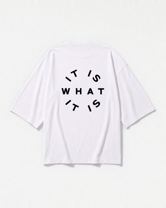 An 'It is what it is' circular stamp graphic printed across the back of a white oversized t-shirt by Dear India